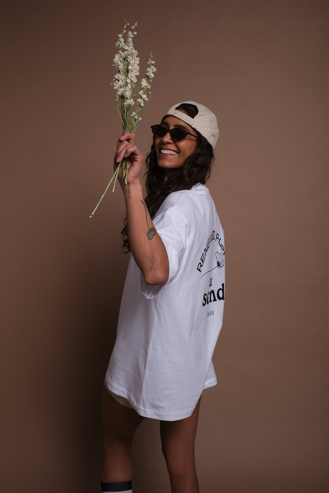 Woman holding flowers and wearing  SEND and Renewed Poppy's limited edition t-shirt with SEND's cherry design. 
