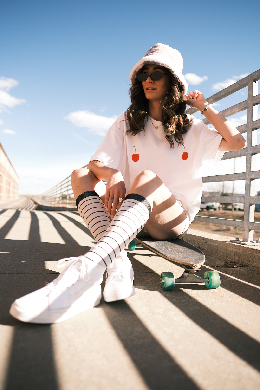 A person sitting on a skateboard wearing SEND and Renewed Poppy's limited edition t-shirt with SEND's cherry design. 